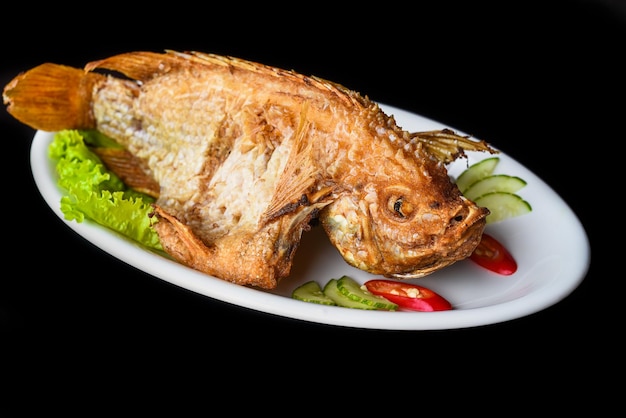 Fish grilled in batter with vegetables and greens on white plate isolated on black background side v