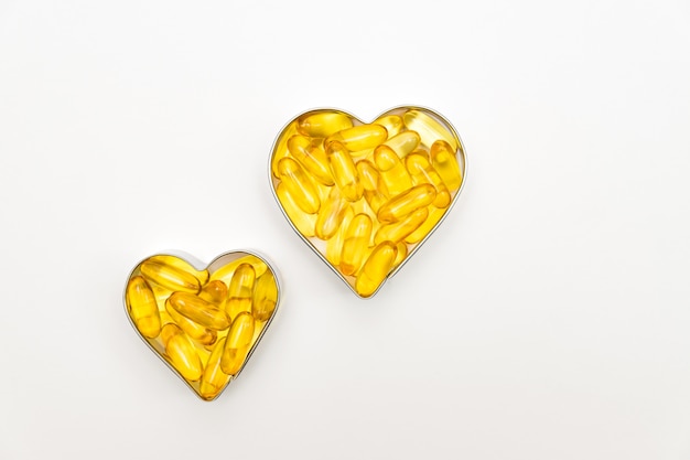 Fish oil capsules in a heart shape boxes on white background, vitamin D supplement, health care concept, top view