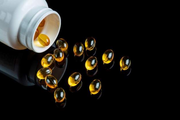 Fish oil capsules in white bottle isolated on black background. Healthy Omega 3 Supplement.