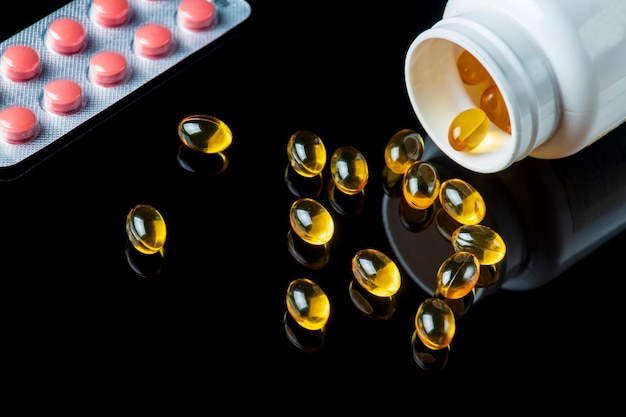 Капсулы рыбьего жира в белой бутылке и таблетки, изолированные на черном фоне Здоровая Омега 3