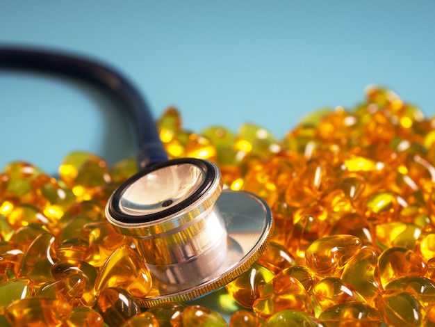 Fish oil capsules with stethoscope on blue background. Healthy omega-3 and stethoscope.