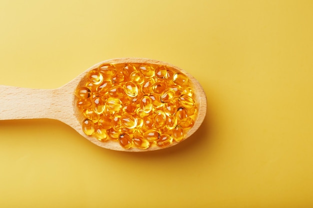 Fish oil capsules in a wooden spoon on a bright yellow background Free space