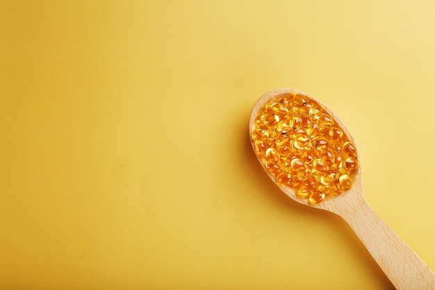 Fish oil capsules in a wooden spoon on a bright yellow background Free space