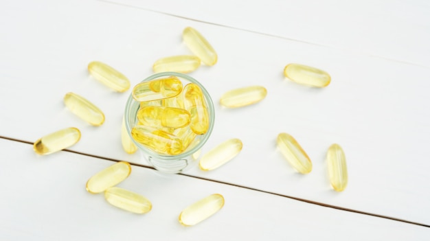 Fish oil in a glass on a white wooden table.