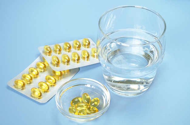 Fish oil omega 3 capsules and glass water on blue table