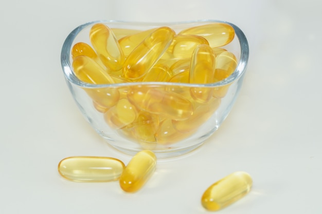 Fish oil pills with omega 3 in a glass bowl on white background.