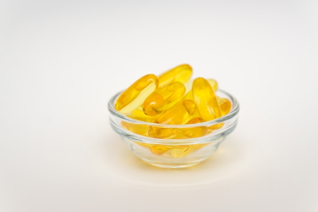 Fish oil supplement, medical and health concept, Soft gel capsules in glass bowl on white wall