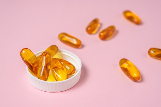 Photo fish oil tablet on light pink background.
