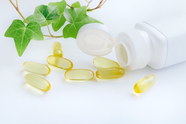 Fish oil vitamin capsules spilling out of pill bottle on white