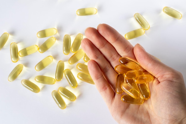 Fish oil in a woman's hand on a white background with scattered capsules