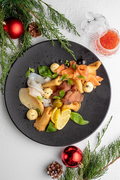 Fish platter on a black plate with red caviar on a light Christmas background with Christmas toys and spruce branches