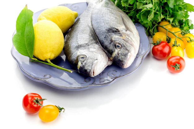 Fish sea breamsSparus aurata on a plate lemons and cherry tomatoes on a white background closeup
