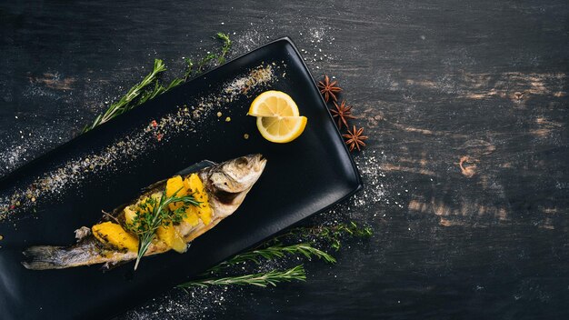 Fish sibas baked with vegetables and citrus fruits On a black wooden background Copy space