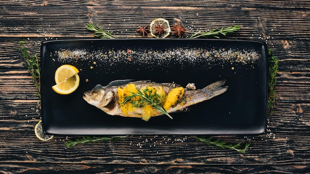 Fish sibas baked with vegetables and citrus fruits On a black wooden background Copy space