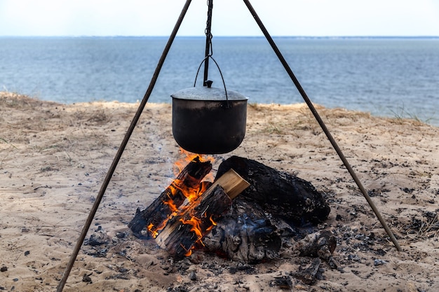 Fish soup cooking in a pot on a fire in the forest by the sea