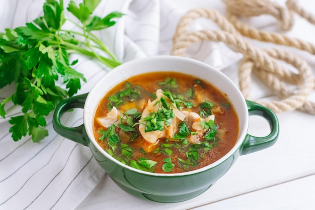 Fish soup with chicken broth with celery and tomatoes large\
ceramic green bowl of hot soup