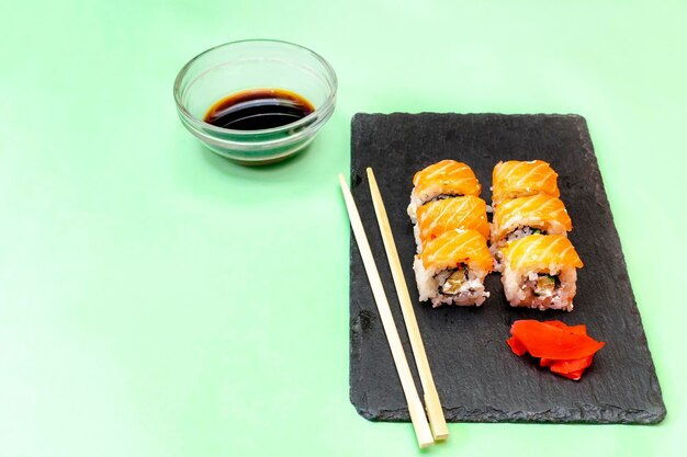 Fish sushi rolls with salmon wasabi and chopsticks on black cutting serving board on green background with copy space Seafood Food service from restaurant concept flatlay