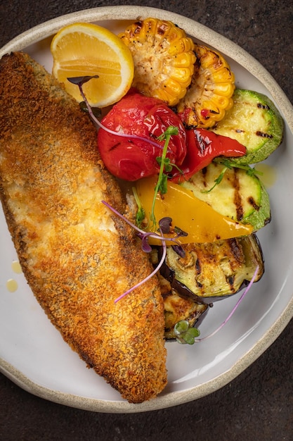 Fish and white plate fried fish fillet and vegetables on black background