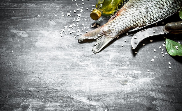 Pesce con un vecchio coltello da intaglio e olio d'oliva. su uno sfondo di legno nero.