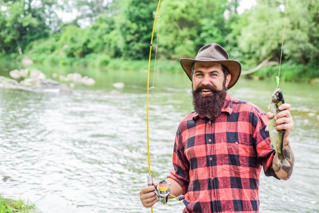 Fisher fishing equipment Rest and recreation Fish on hook Brutal man stand in river water Man bearded fisher Fisher masculine hobby Fishing requires to be mindful and fully present in moment