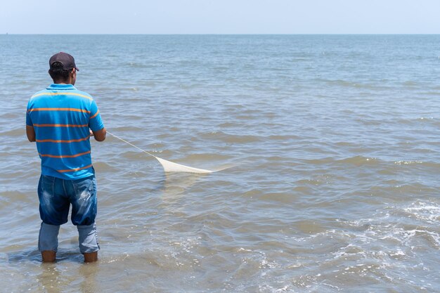 Pescatore sulla spiaggia che recupera una rete da pesca