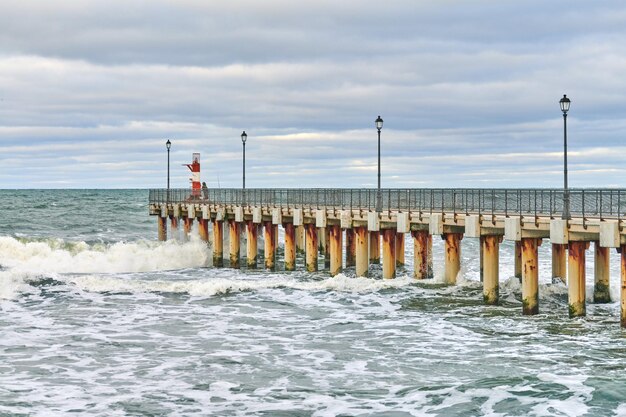 Photo fisherman in camouflage standing and fishing on pier with lighthouse seascape