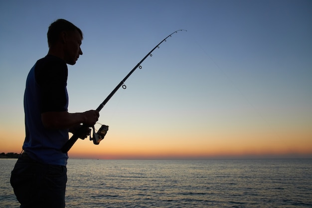Рыбак рыб на силуэт озера на закате
