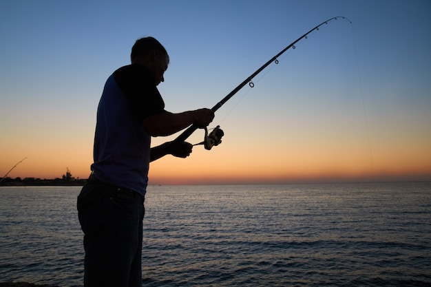 漁師は湖で釣りをします。日没時のシルエット