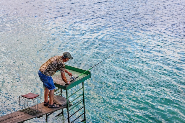 Premium Photo  A fisherman is fishing by spinning on the river bank  standing on a wooden platform