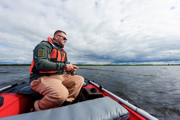 A fisherman is sitting in an inflatable motor boat with a spinning rod Professional fishing on the lake