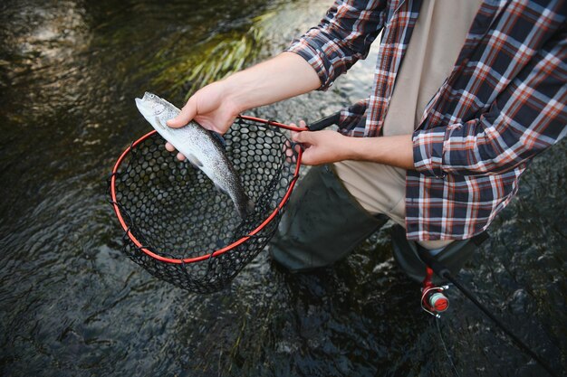 Fisherman picking up big rainbow trout from his fishing net