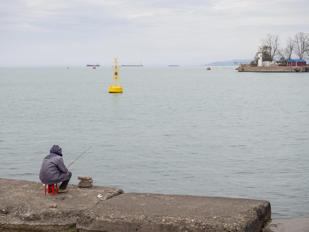 海岸の桟橋にいる漁師 男が釣り竿を持って浜辺に座っている