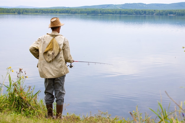 A fisherman on the shore of a picturesque lake is fishing with a fishing rod in summer