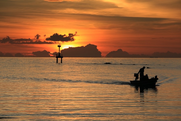 漁師のシルエットのボートは海と夕日の灯台の灯台に戻ります