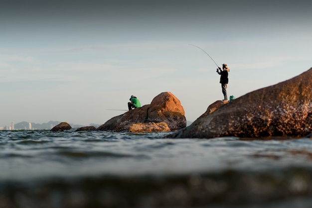 The fisherman silhouette on the rock at the sea