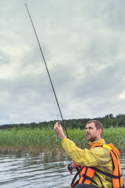 Fisherman sitting in an old wooden boat and fishing on a cloudy day.