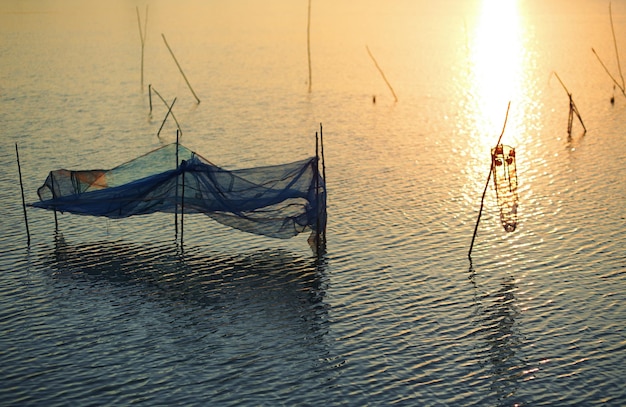 A fisherman stands in the water with a net in the foreground.