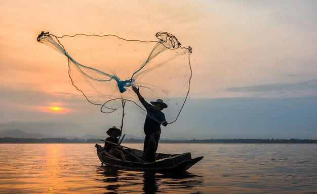 Fisherman throwing net in sea during sunset