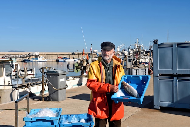 Pescatore con una scatola di pesce all'interno di una barca da pesca