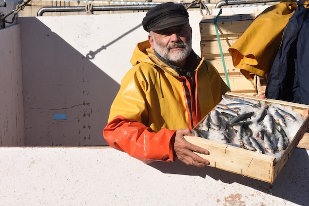 Pescatore con una scatola di pesce all'interno di una barca da pesca