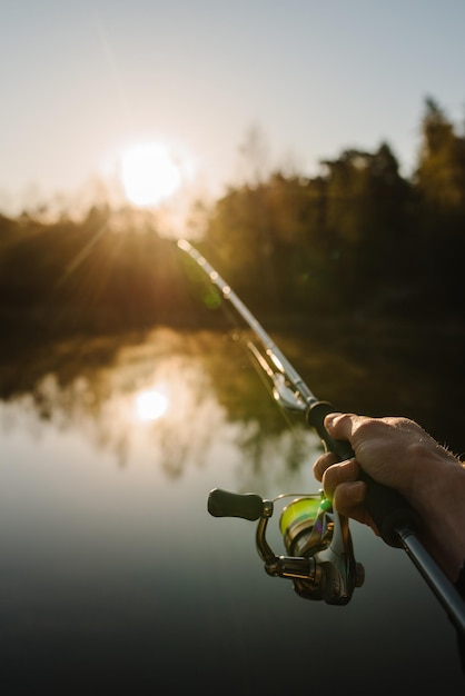 Fisherman with rod spinning reel on the river bank sunrise\
fishing for pike perch carp fog against the backdrop of lake\
background misty morning wild nature the concept of a rural\
getaway