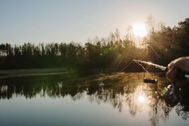 Photo fisherman with rod spinning reel on the river bank sunrise fishing for pike perch carp fog against the backdrop of lake background misty morning wild nature the concept of a rural getaway