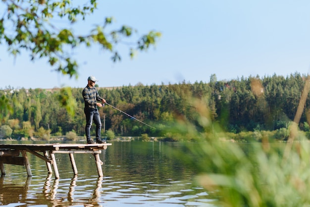 Pescatore con canna, mulinello da spinning sulla riva del fiume