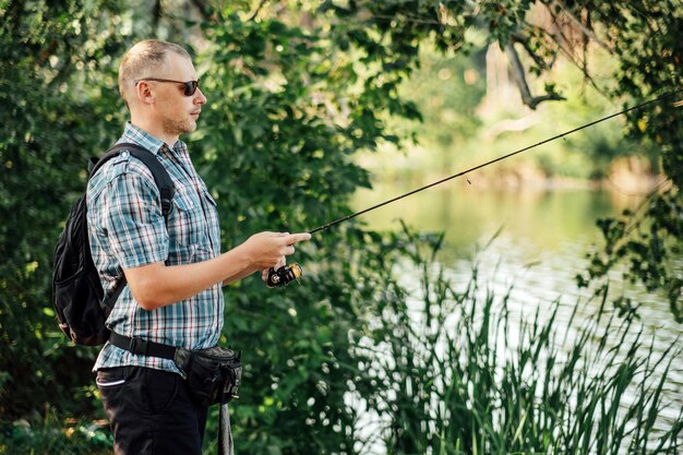 Pescatore con canna da spinning sul lago estivo pescatore con la filatura nelle sue mani che cattura il pesce a