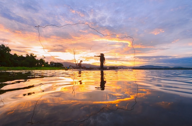 Photo fisherman on wooden boat casting a net for catching freshwater fish in reservoir.