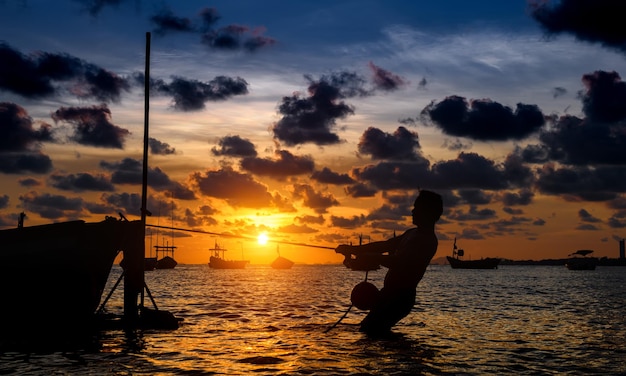 Fisherman and wooden boat in the sea shore with sunset time warm lighting dark