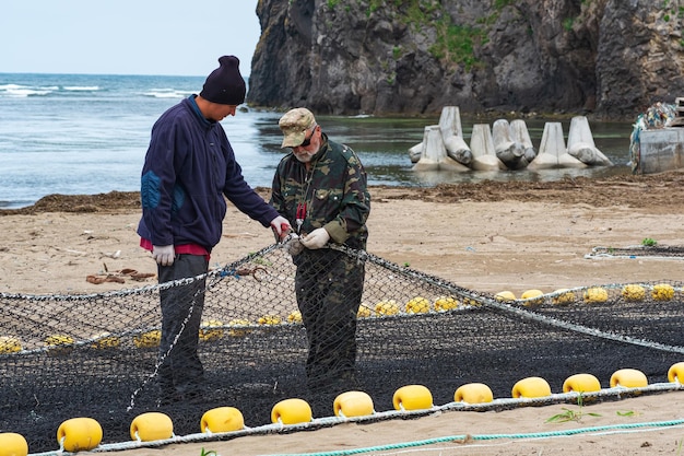 漁師は海岸で漁網をチェックして修理します