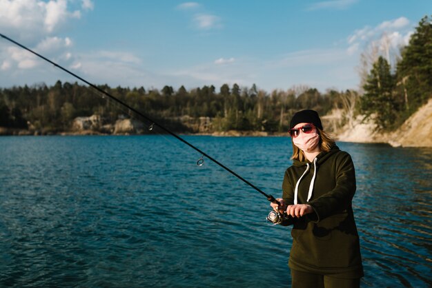 Fisherwoman, rod, spinning reel on lake bank. Quarantine concept in countryside.