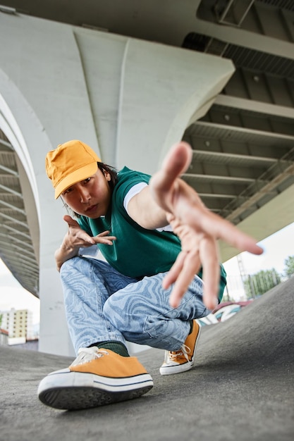 Fisheye of young asian man dancing outdoors and gesturing to camera wearing colorful street style cl