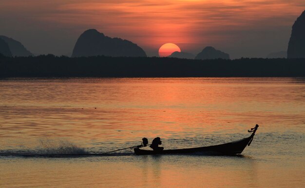 A fishing boat silhouette is sailing in a lake with sun is rising in background